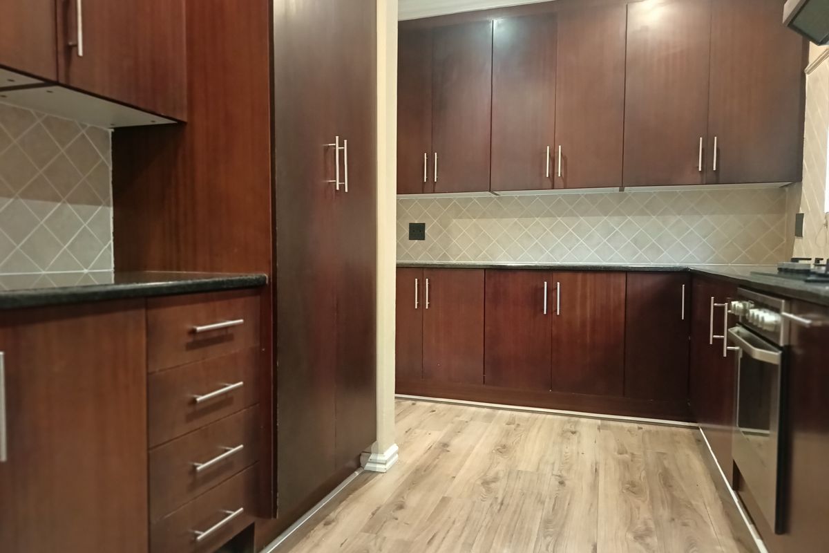 A clean, functional kitchen featuring dark wood cabinetry, granite countertops, a tiled backsplash, and built-in oven with hob.