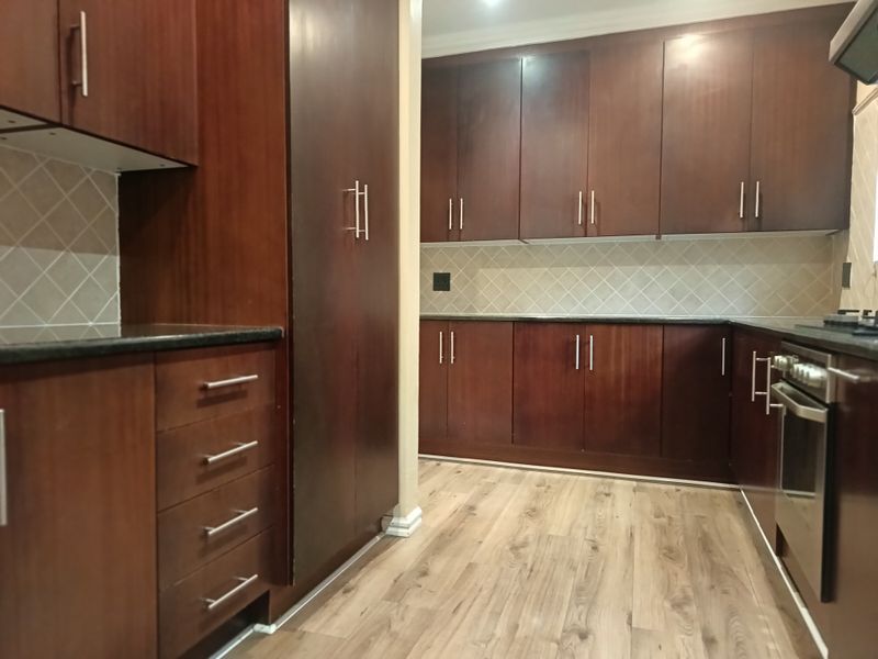 A clean, functional kitchen featuring dark wood cabinetry, granite countertops, a tiled backsplash, and built-in oven with hob.