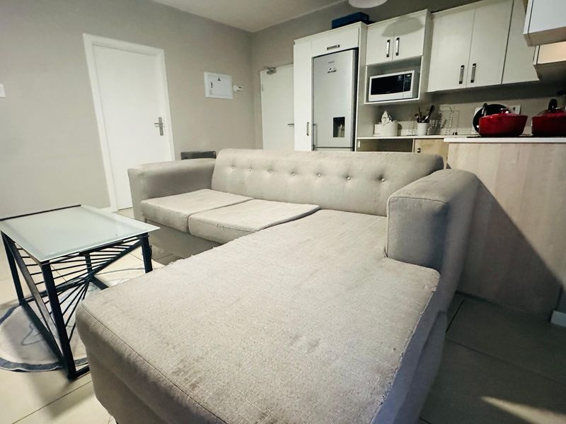 Open-plan living area featuring tiled flooring and a compact kitchen with built-in cabinetry and integrated appliances.