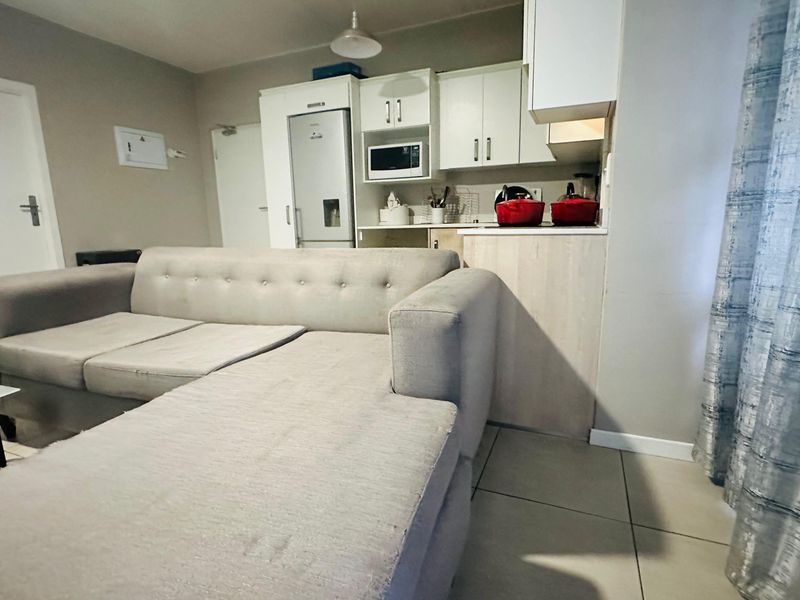 Open-plan living area featuring a compact kitchen with built-in cabinetry and tiled flooring, seamlessly integrated with the lounge space.