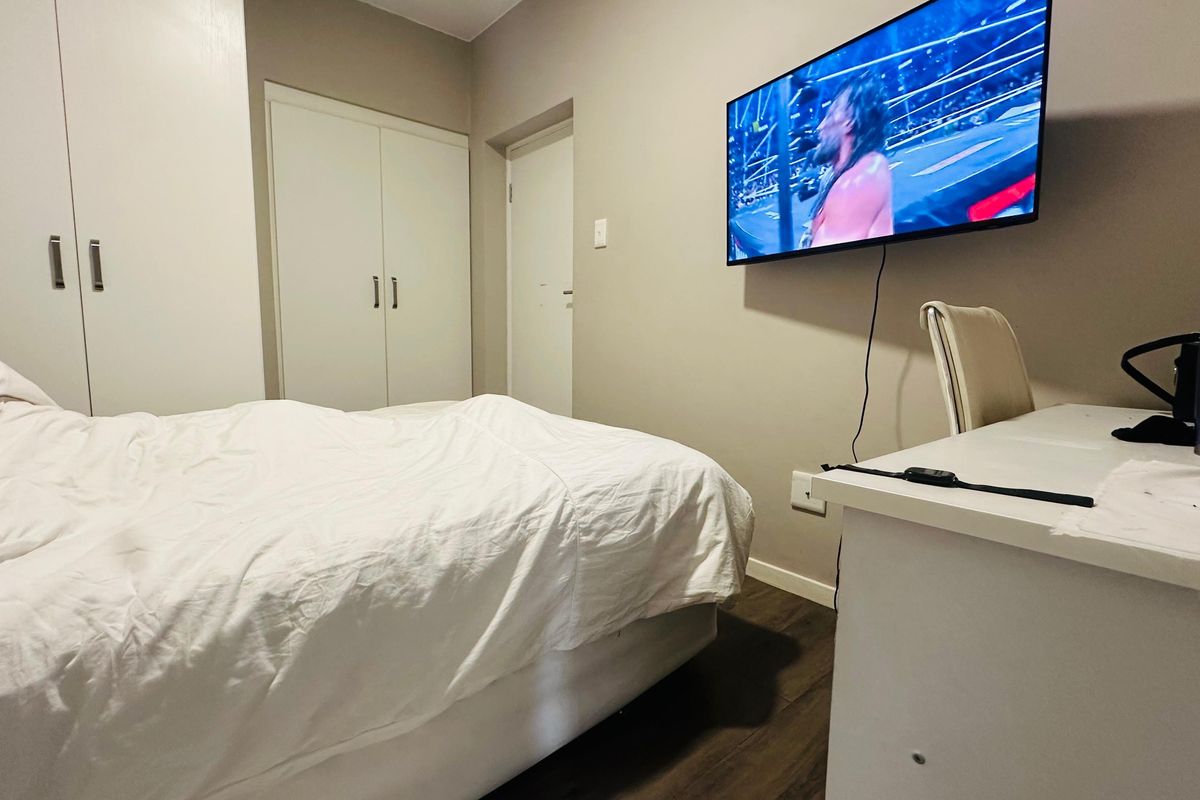 A functional bedroom featuring built-in cupboards, laminate flooring, and a wall-mounted television, providing a practical and comfortable living space.