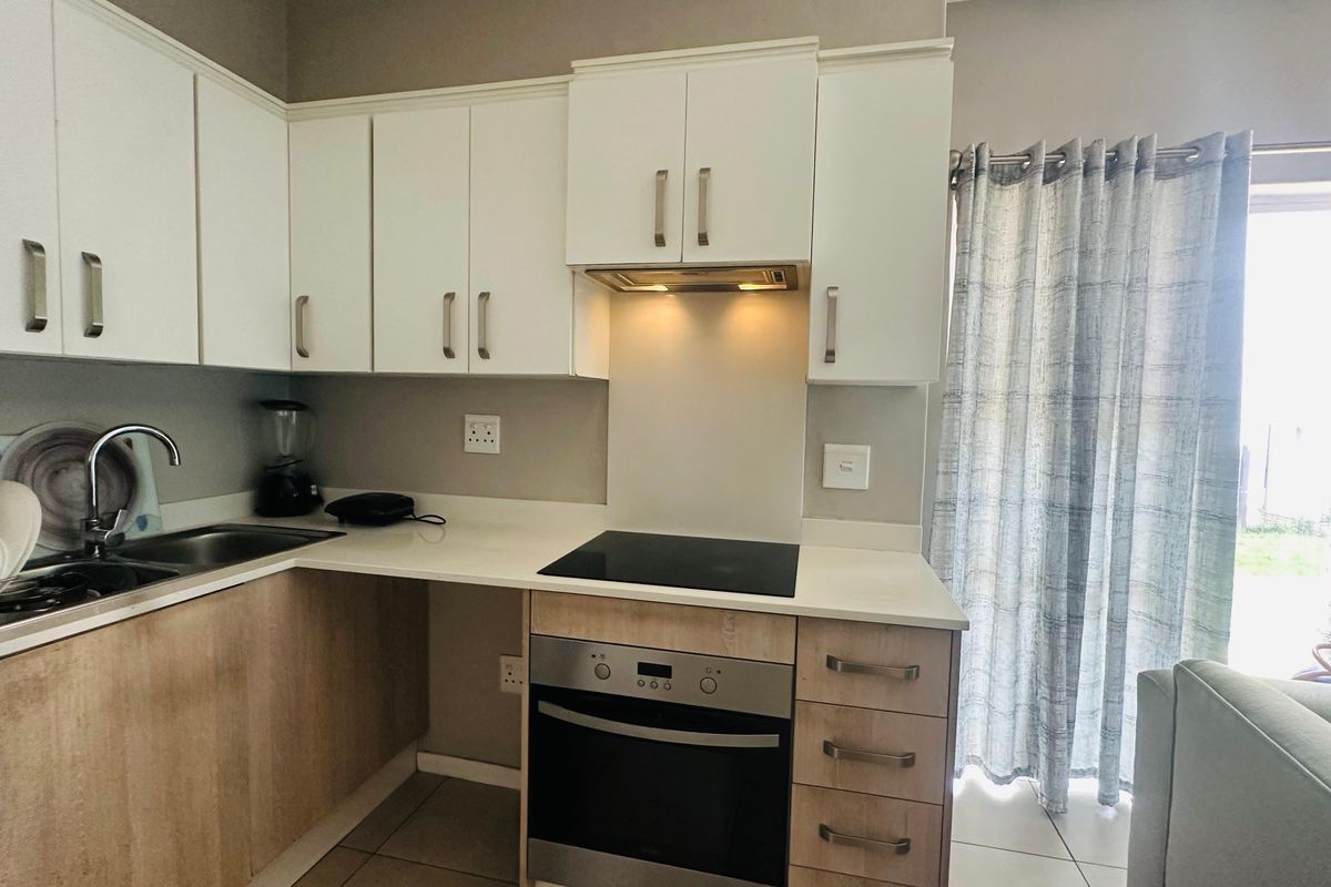 Modern kitchen featuring white upper cabinetry, wood-finish lower cabinets, stone countertops, integrated electric hob, oven, and extractor fan with tiled flooring.