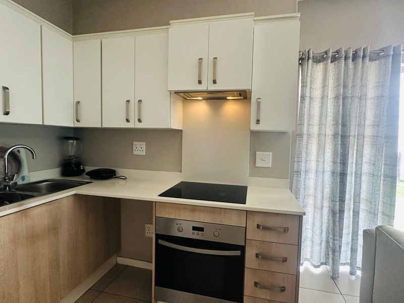 Modern kitchen featuring white upper cabinetry, wood-finish lower cabinets, stone countertops, integrated electric hob, oven, and extractor fan with tiled flooring.
