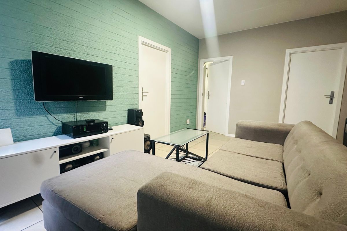 A living room featuring a textured green accent wall, tiled flooring, and multiple internal doors, providing a functional and neutral living space.