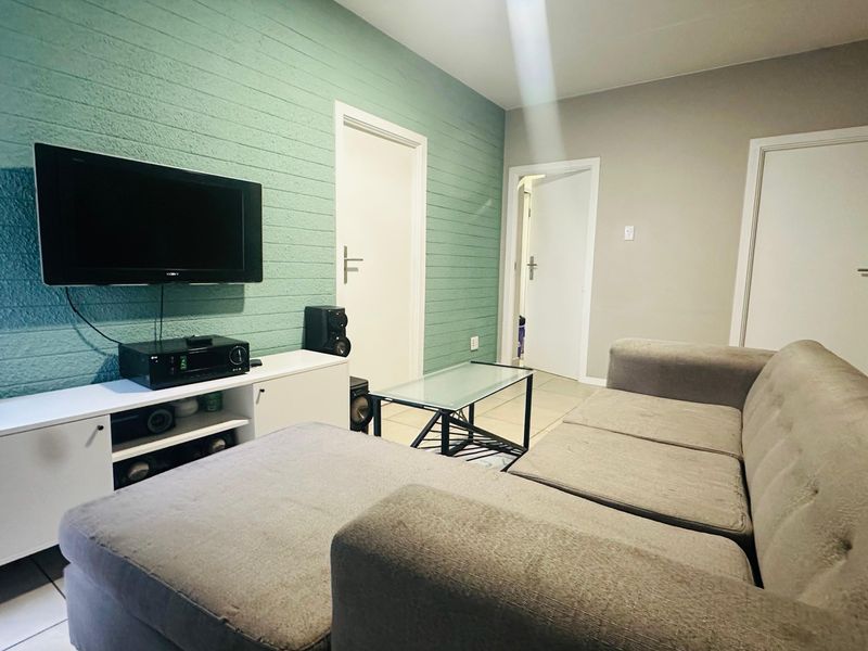 A living room featuring a textured green accent wall, tiled flooring, and multiple internal doors, providing a functional and neutral living space.