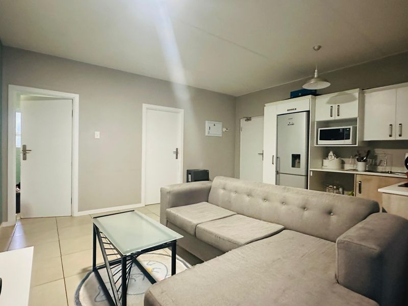 Open-plan living area featuring tiled flooring and a functional kitchen with built-in cabinetry, seamlessly connecting the lounge and kitchen spaces.