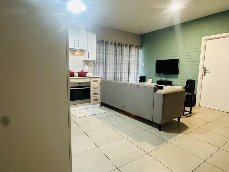 Open-plan living area featuring tiled flooring, a textured accent wall, and a compact kitchen with built-in cabinetry and oven.