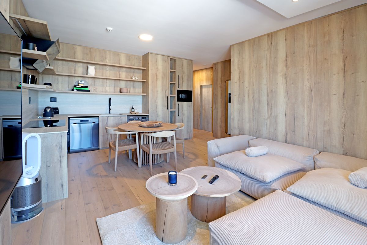 Modern open-plan living area featuring light wood cabinetry, integrated kitchen appliances, and seamless wood-look flooring throughout the space.