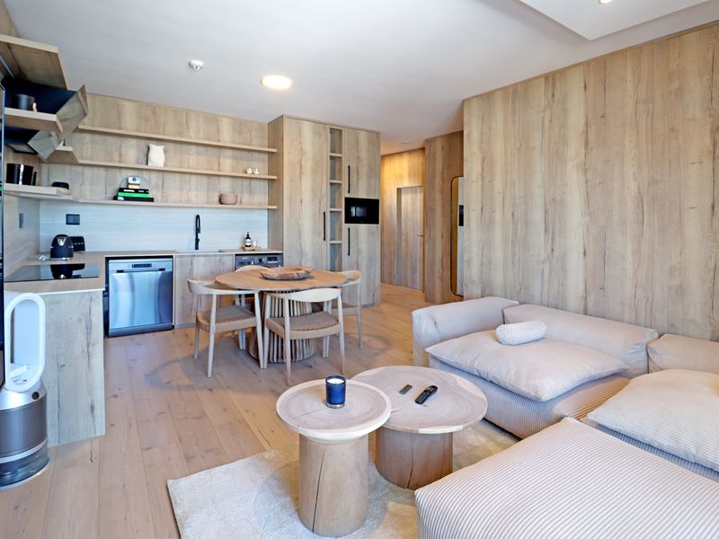 Modern open-plan living area featuring light wood cabinetry, integrated kitchen appliances, and seamless wood-look flooring throughout the space.
