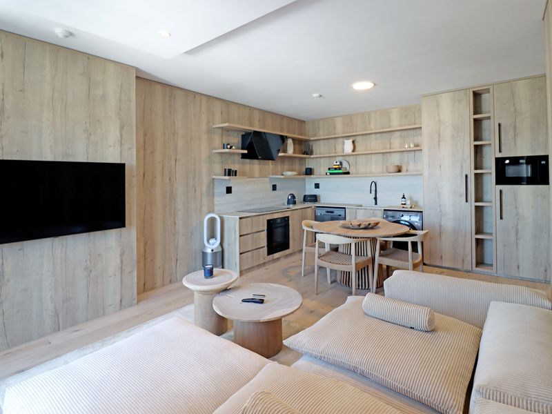 Modern open-plan living area featuring light wood cabinetry, integrated kitchen appliances, and a seamless flow between the kitchen and lounge space.