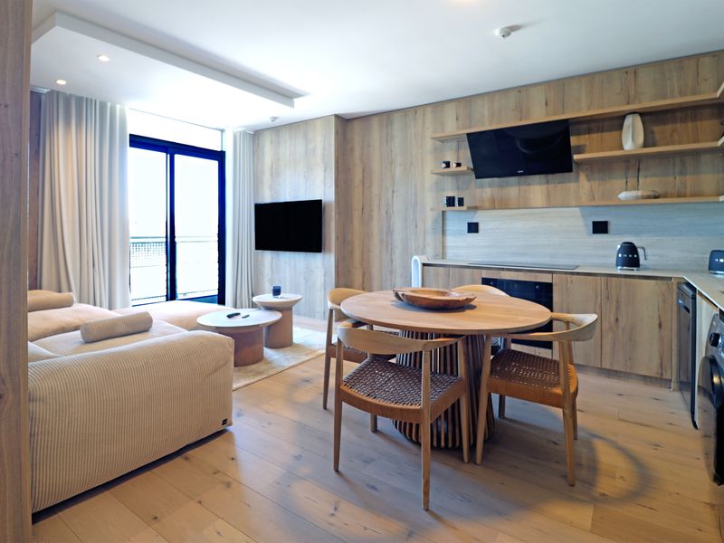 Modern open-plan living area featuring light wood cabinetry, integrated kitchen appliances, and seamless flow to a private balcony.
