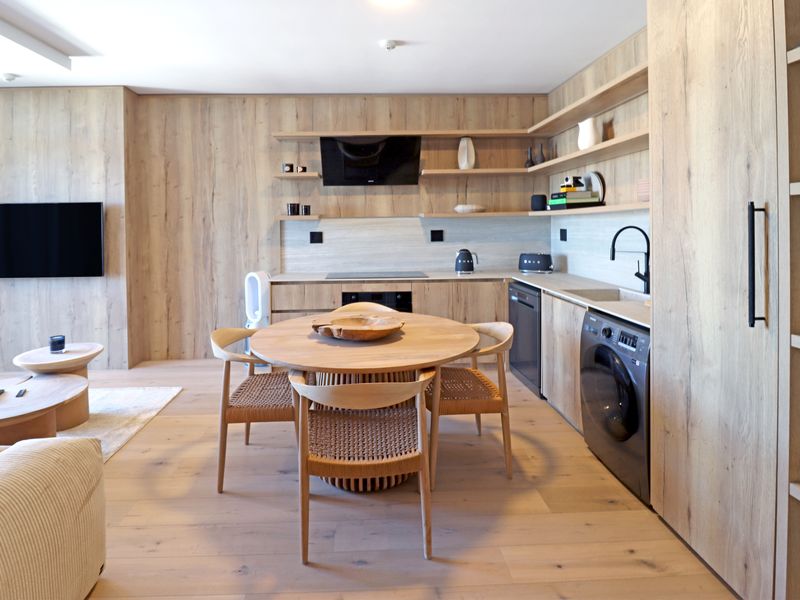 Modern open-plan kitchen featuring light wood cabinetry, integrated appliances, sleek shelving, and a seamless transition into the living area.