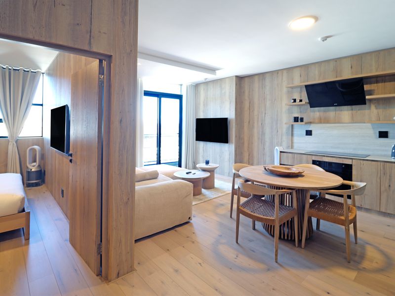 Modern open-plan apartment featuring light wood-look cabinetry, integrated kitchen appliances, and seamless flow between the living, dining, and bedroom areas.