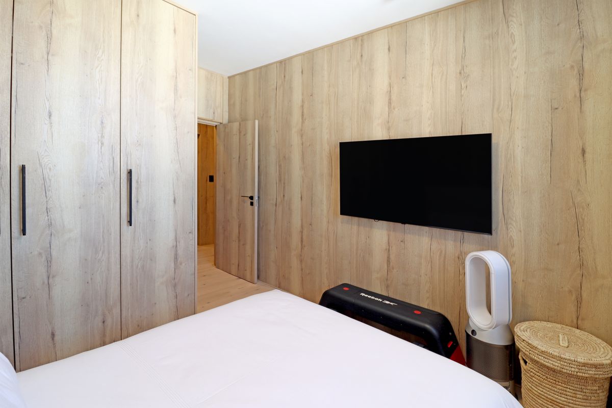 Modern bedroom featuring light wood-grain wall paneling, integrated floor-to-ceiling cabinetry, and a wall-mounted television.