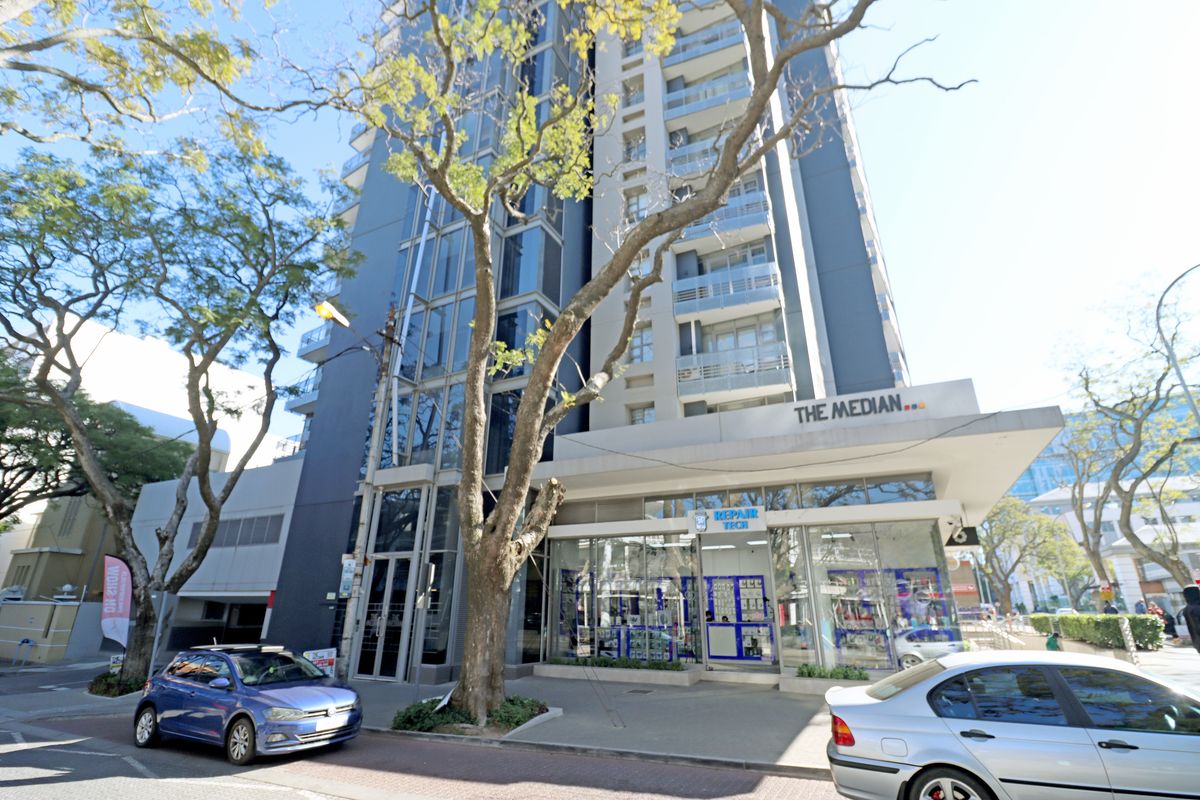 Exterior view of The Median apartment building, featuring a modern glass and concrete facade with ground-floor commercial retail space.