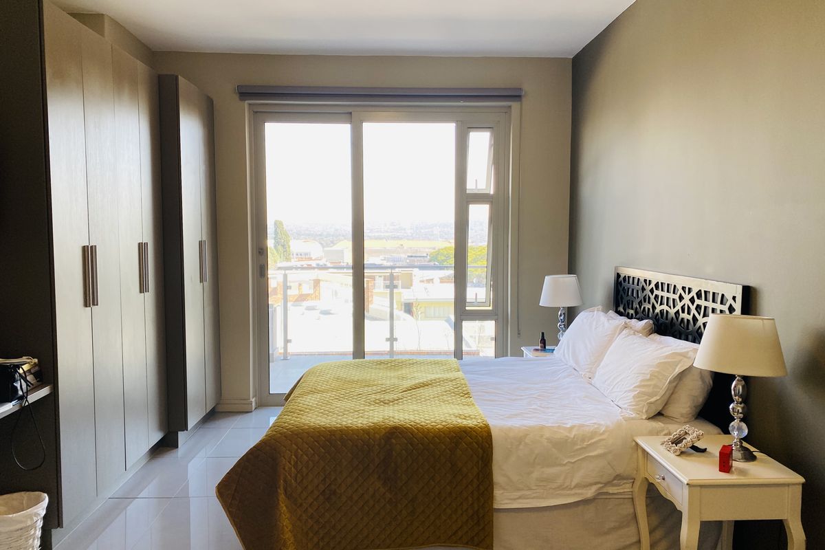 A well-maintained bedroom featuring built-in floor-to-ceiling wardrobes, tiled flooring, and a sliding glass door providing access to a balcony with urban views.