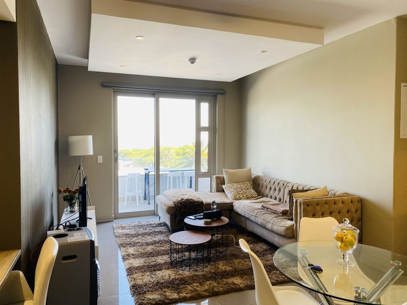 Open plan living and dining area featuring a recessed ceiling with downlights and large sliding glass doors leading to a balcony.
