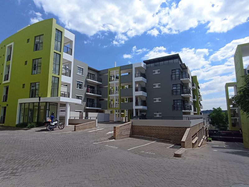 Exterior view of a modern multi-story apartment complex featuring paved driveway access, balconies, and contemporary architectural design.