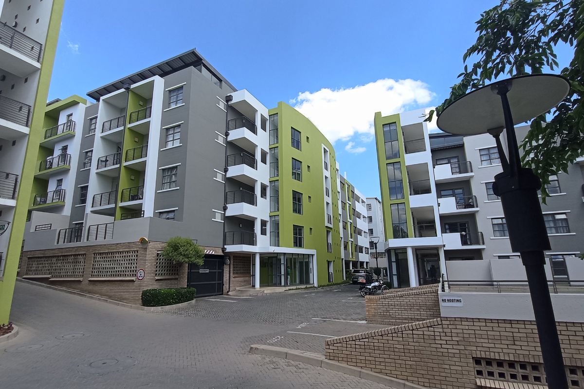 Exterior view of a modern multi-story apartment complex featuring paved driveway access, balconies, and contemporary architectural design.