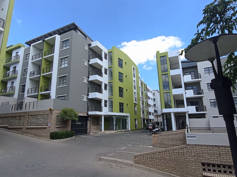 Exterior view of a modern multi-story apartment complex featuring paved driveway access, balconies, and contemporary architectural design.