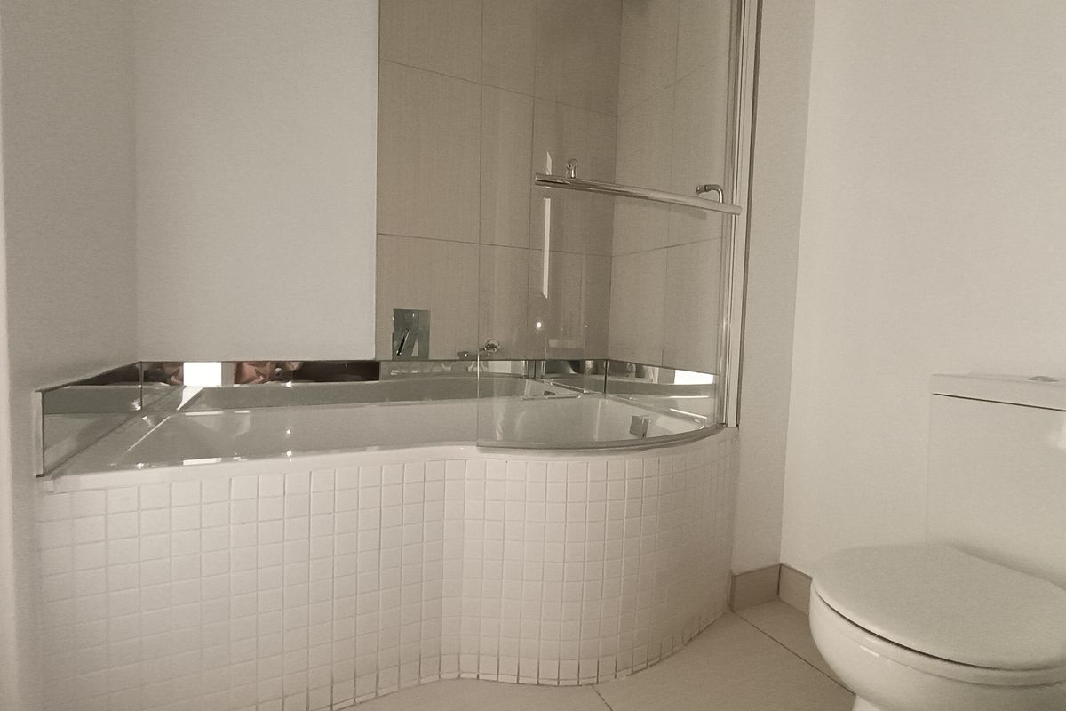 A clean, modern bathroom featuring a built-in bathtub with a glass shower screen, tiled surround, and a standard toilet.