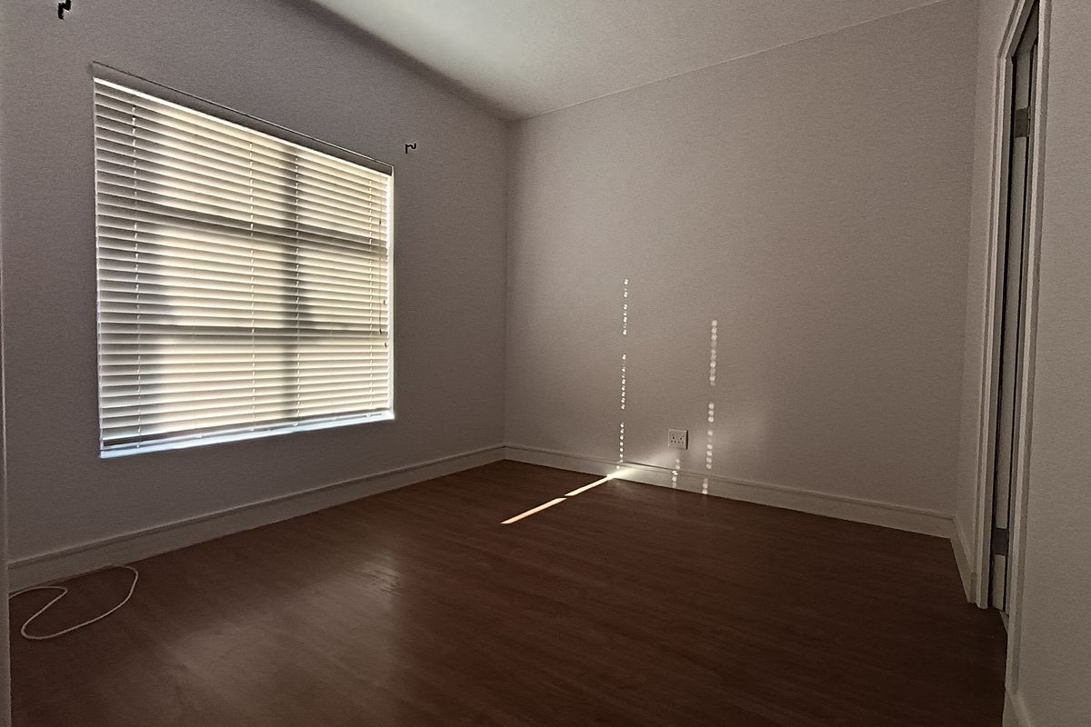 A bright, empty bedroom featuring laminate flooring, neutral walls, and venetian blinds, offering a clean and versatile space ready for personalization.