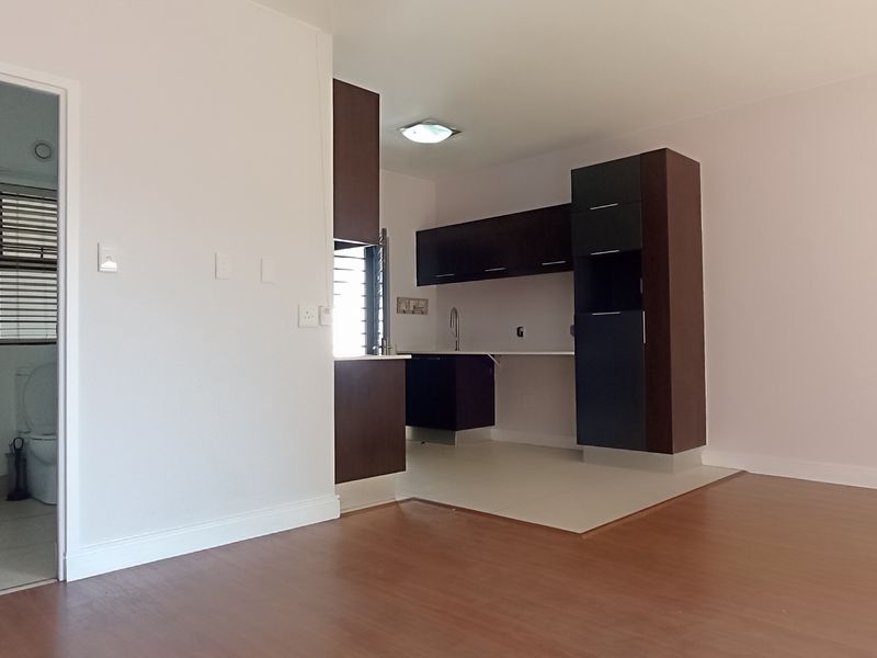 An open-plan living area featuring a compact kitchen with dark cabinetry and an adjacent bathroom equipped with a shower and toilet.