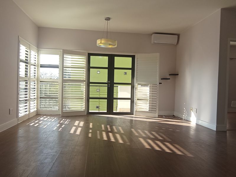 Spacious, light-filled living area featuring modern laminate flooring, plantation shutters, and a wall-mounted air conditioning unit, offering a clean and neutral canvas.