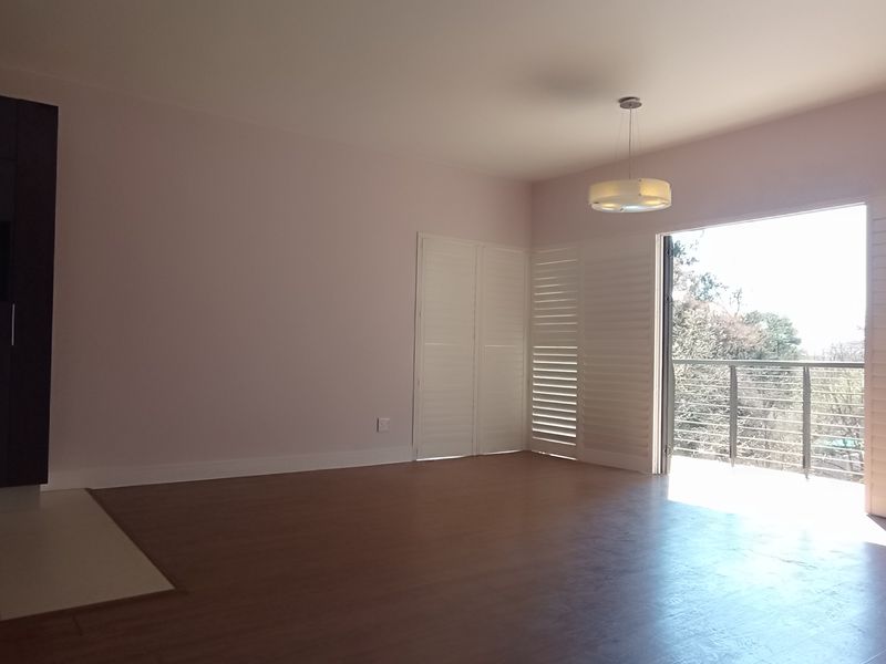 Spacious open-plan living area featuring laminate flooring, built-in cabinetry, air conditioning, and plantation shutters opening onto a balcony.