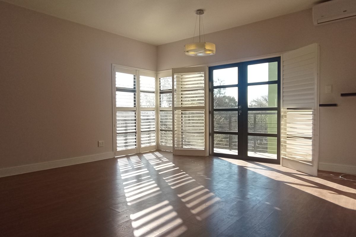 Spacious living area featuring laminate flooring, plantation shutters, and a split-system air conditioner, with direct access to an outdoor balcony.