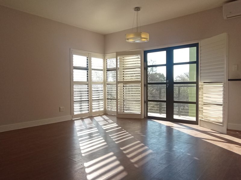 Spacious living area featuring laminate flooring, plantation shutters, and a split-system air conditioner, with direct access to an outdoor balcony.
