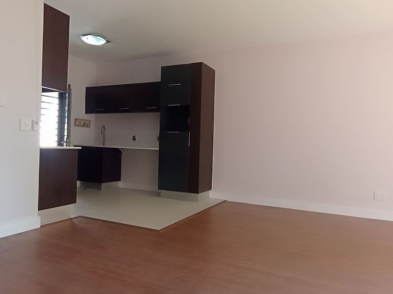 An open-plan living and kitchen area featuring dark wood cabinetry, laminate flooring, and a neutral color palette, offering a clean and versatile living space.