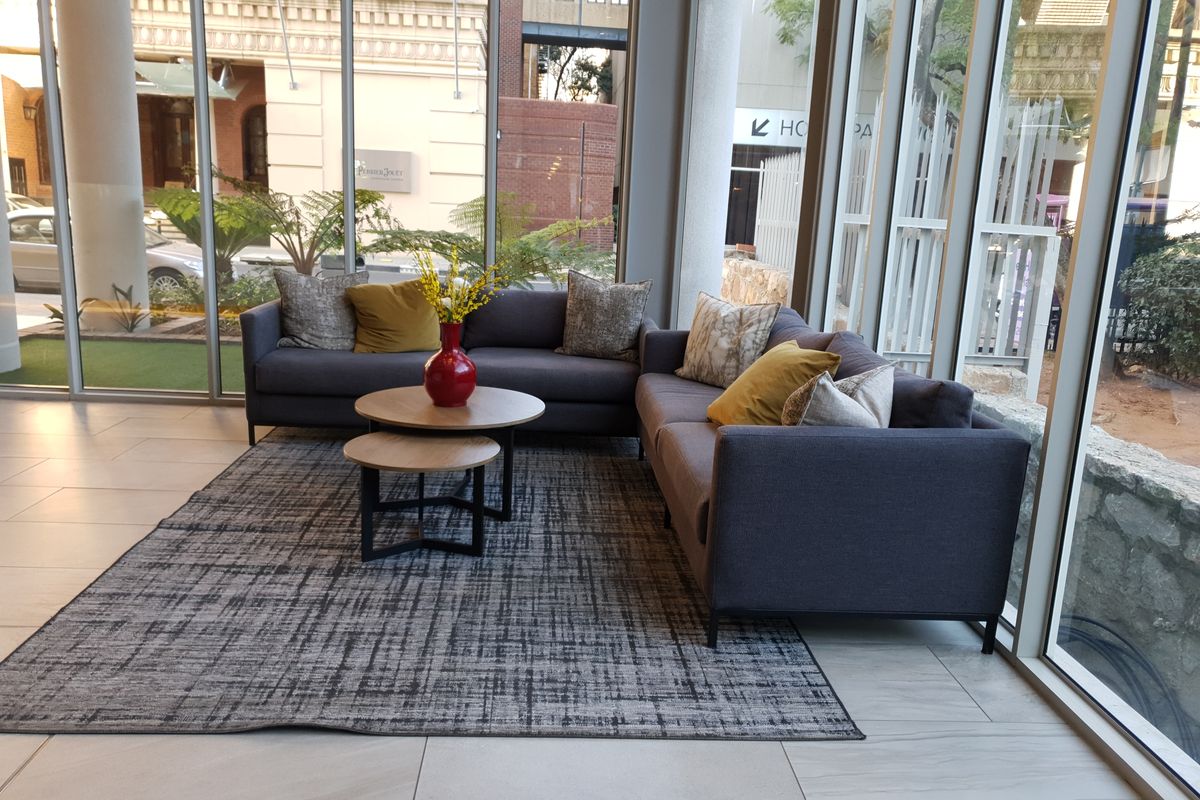 A bright living area featuring expansive floor-to-ceiling windows, modern tiled flooring, and structural columns, offering a contemporary and open atmosphere.