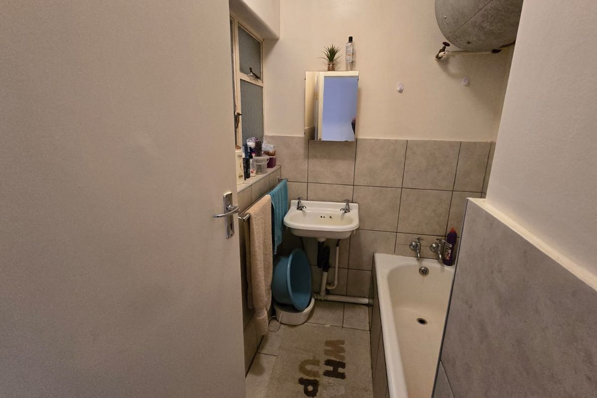 A compact bathroom featuring a standard bathtub, wall-mounted basin, and exposed plumbing fixtures, requiring cosmetic updates to modernize the space.