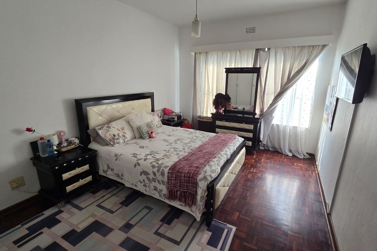 A bedroom featuring parquet flooring, large window with curtains, and a ceiling light fixture.