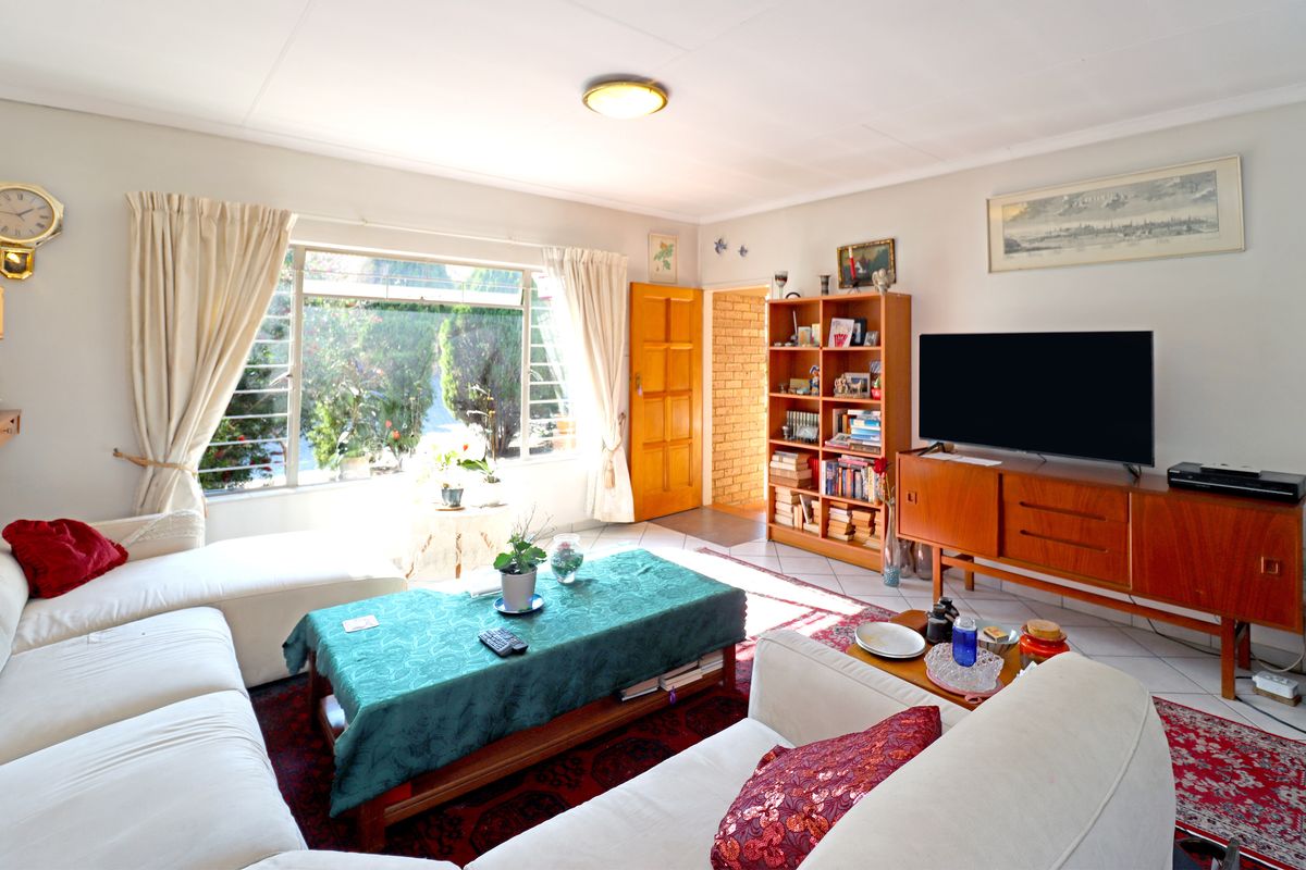 A bright living room featuring tiled flooring, a large window providing natural light, and a wooden door leading to an adjacent space.