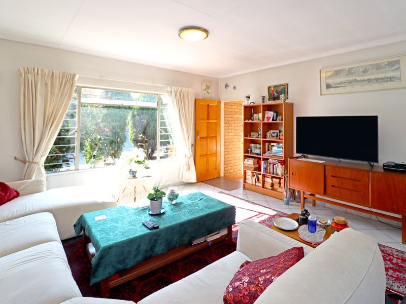 A bright living room featuring tiled flooring, a large window providing natural light, and a wooden door leading to an adjacent space.