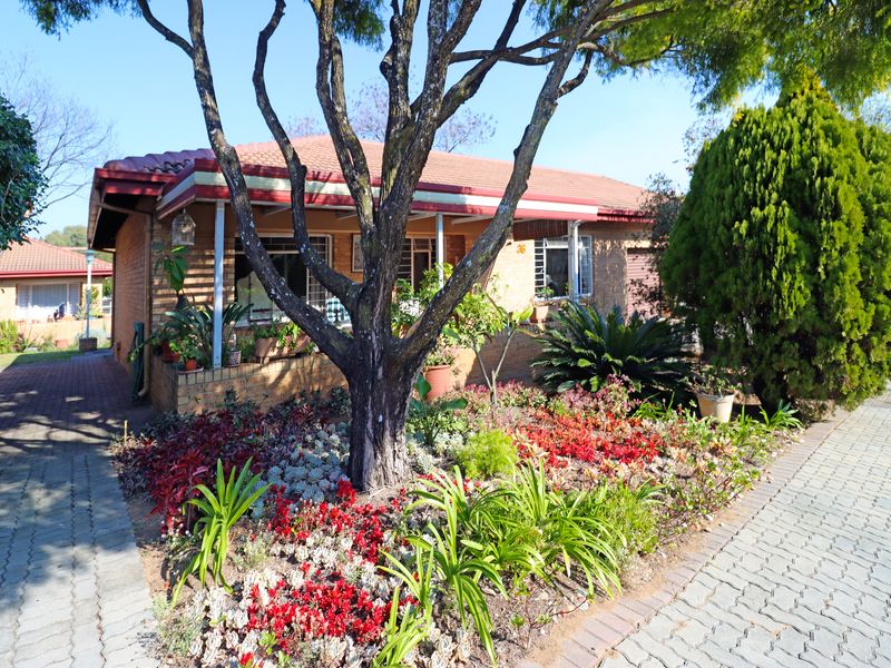 Front view of a brick townhouse featuring a covered patio, a well-maintained landscaped garden, and a paved driveway.