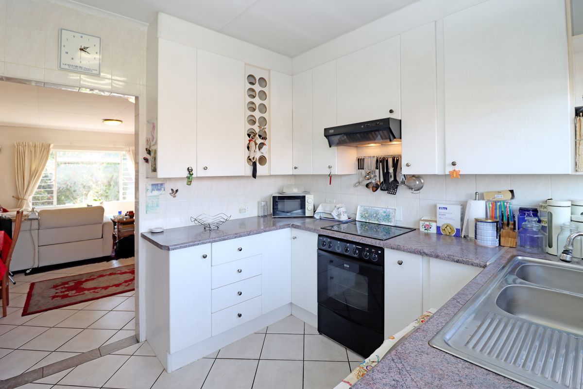 A functional kitchen featuring white cabinetry, laminate countertops, a built-in oven with hob, and tiled flooring, with an open flow to the adjacent living area.