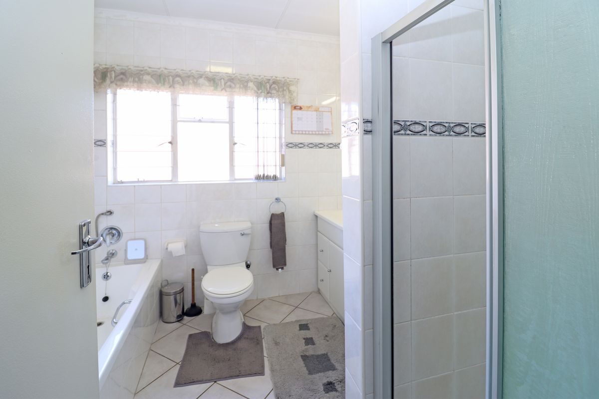 A functional bathroom featuring a bathtub, separate shower enclosure, toilet, and vanity cabinet with tiled finishes throughout.