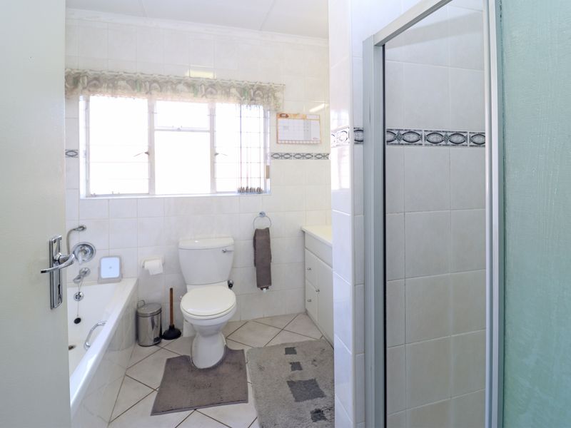 A functional bathroom featuring a bathtub, separate shower enclosure, toilet, and vanity cabinet with tiled finishes throughout.
