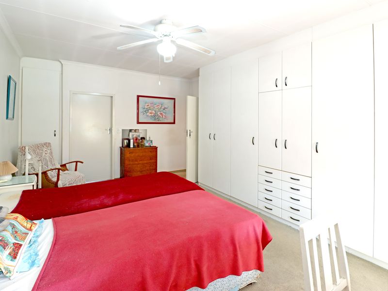 A bedroom featuring extensive white built-in cupboards with integrated drawers and a ceiling fan.