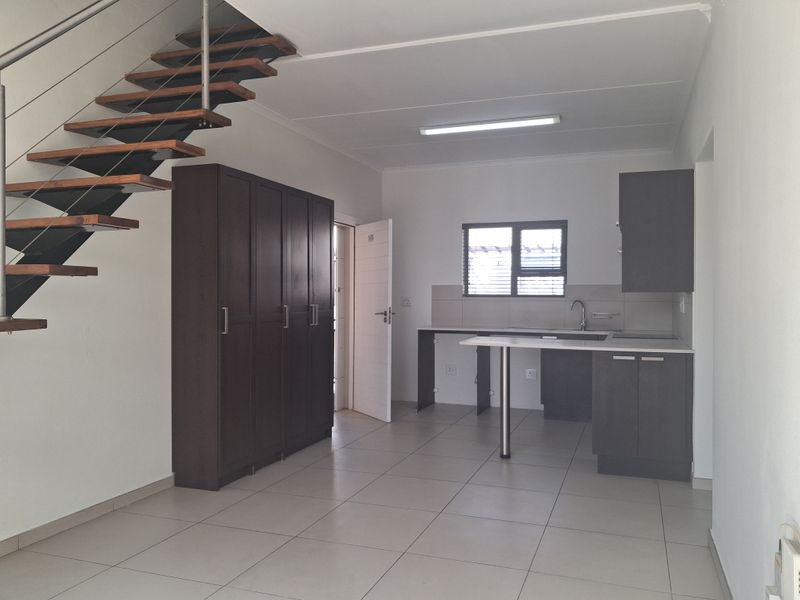 Open plan living area featuring a modern floating staircase, tiled flooring, and a compact kitchen with built-in cabinetry.