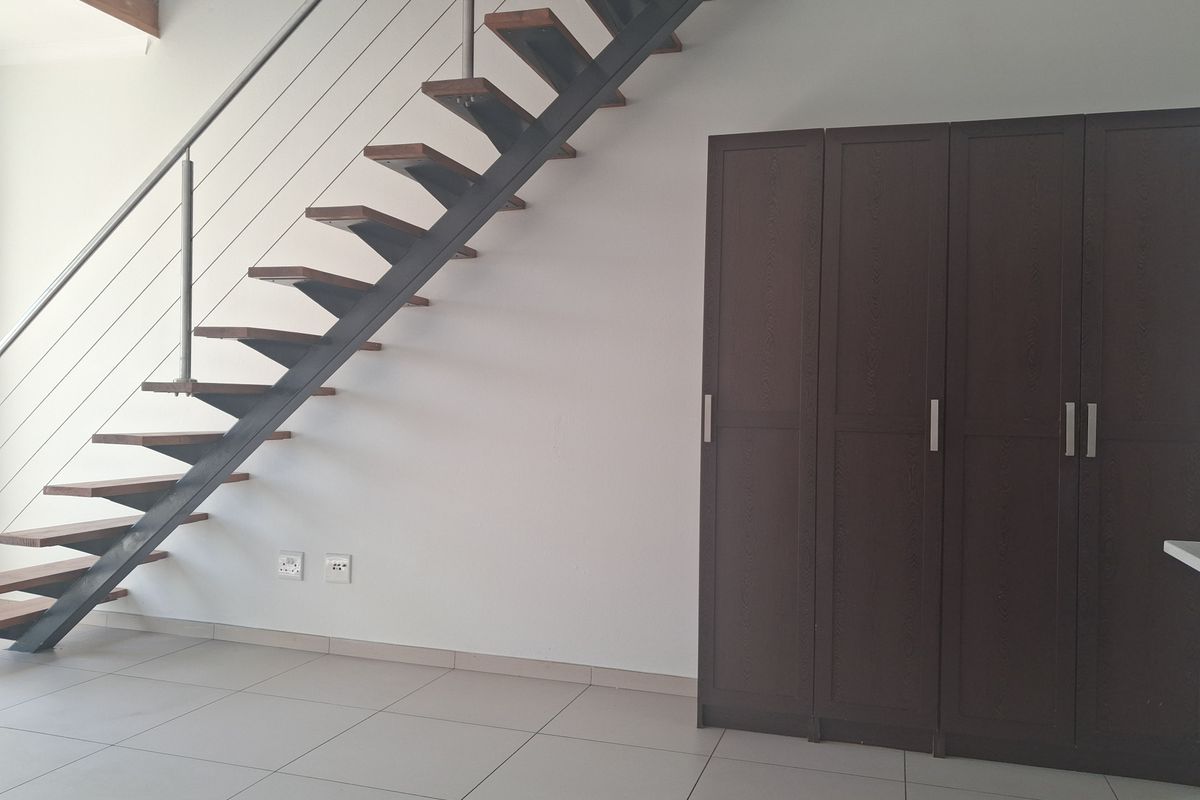 Open-plan living area featuring a modern open-tread staircase with stainless steel balustrades and built-in storage cupboards on tiled flooring.