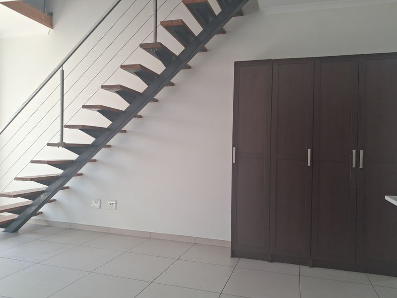 Open-plan living area featuring a modern open-tread staircase with stainless steel balustrades and built-in storage cupboards on tiled flooring.