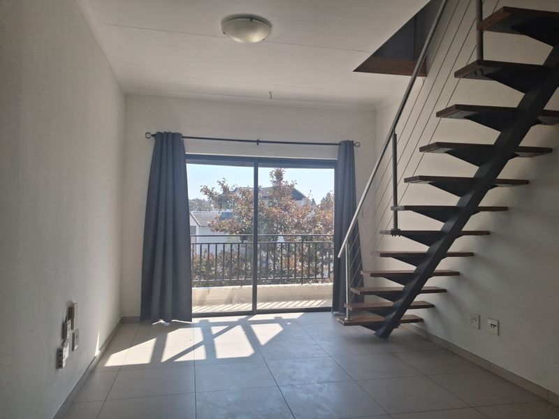 An empty living room featuring tiled flooring, an open-tread staircase with metal balustrades, and a sliding glass door leading to a balcony.