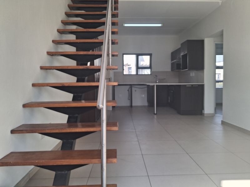 Open plan living area featuring a modern staircase with timber treads and stainless steel balustrade, leading to a functional kitchen space with tiled flooring.