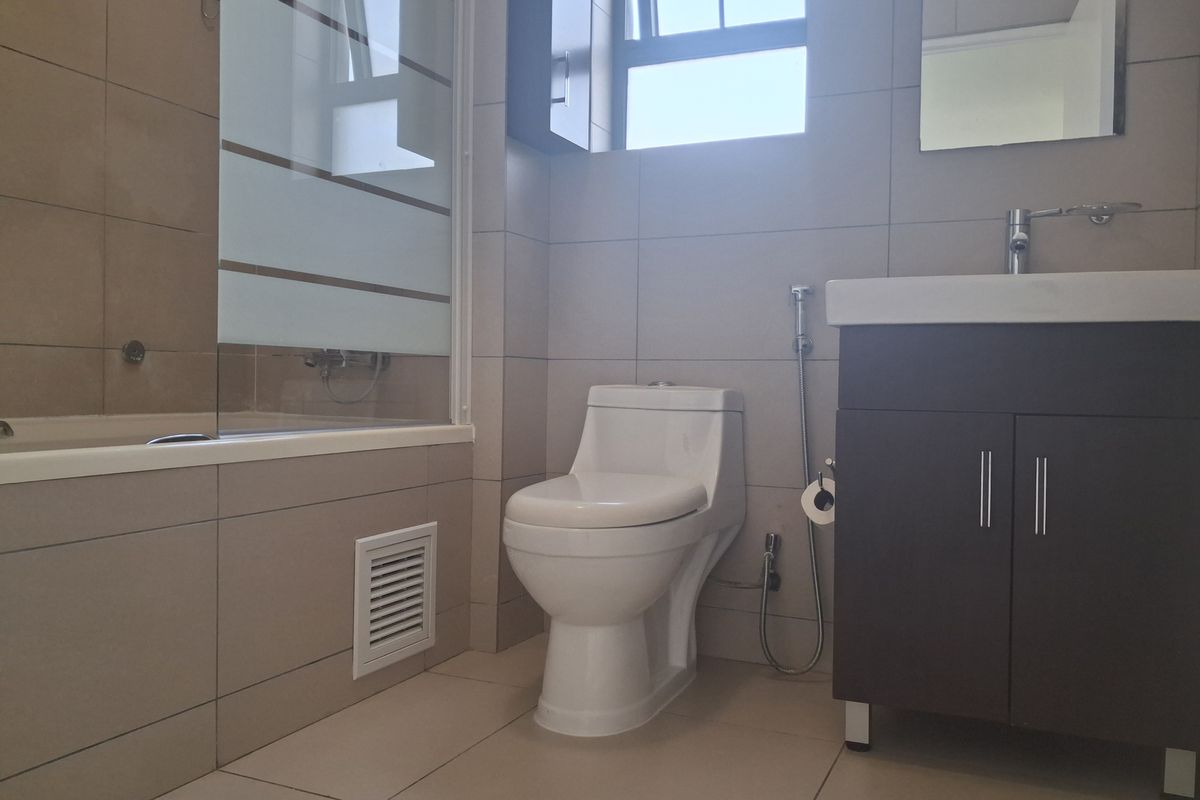 A clean, modern bathroom featuring a bathtub with a glass screen, a vanity unit with a washbasin, and a toilet with a bidet spray.