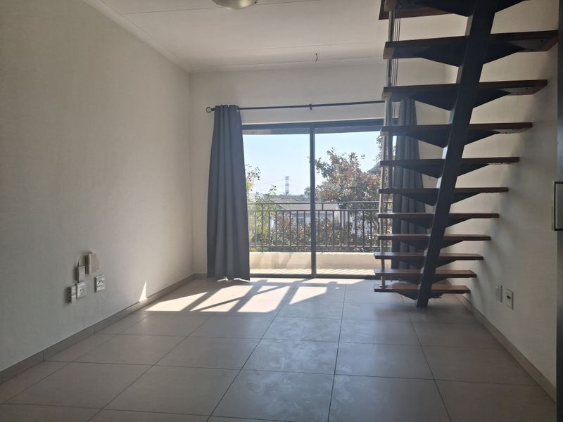 An open-plan living area featuring tiled flooring, a modern metal staircase, and a sliding glass door leading to a balcony.