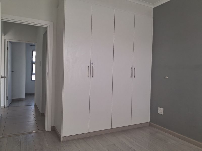 A clean, empty bedroom featuring modern laminate flooring, a large white built-in wardrobe, and a neutral grey accent wall.
